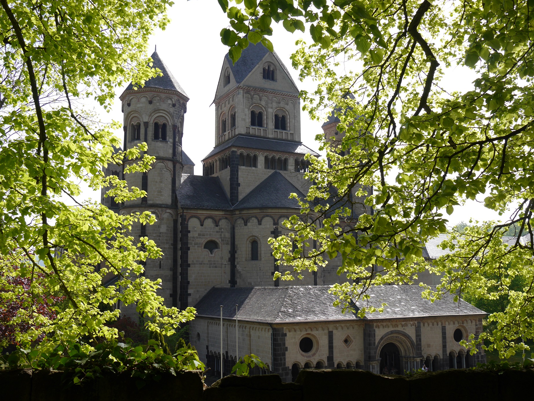 Durch die Bäume mit grünen Blättern ist die Abteikirche Maria Laach zu sehen.